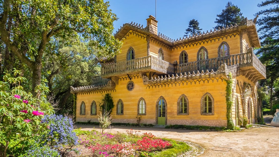 Quinta da Regaleira's yellow villa surrounded by lush gardens in Sintra, Portugal.