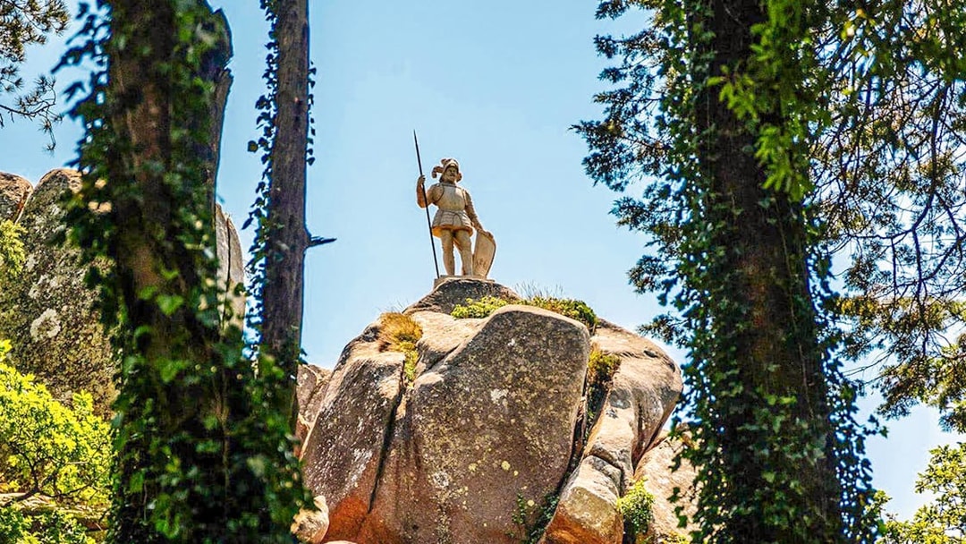 Statue of the Warrior on a rocky hill in Pena Palace Park, surrounded by trees.
