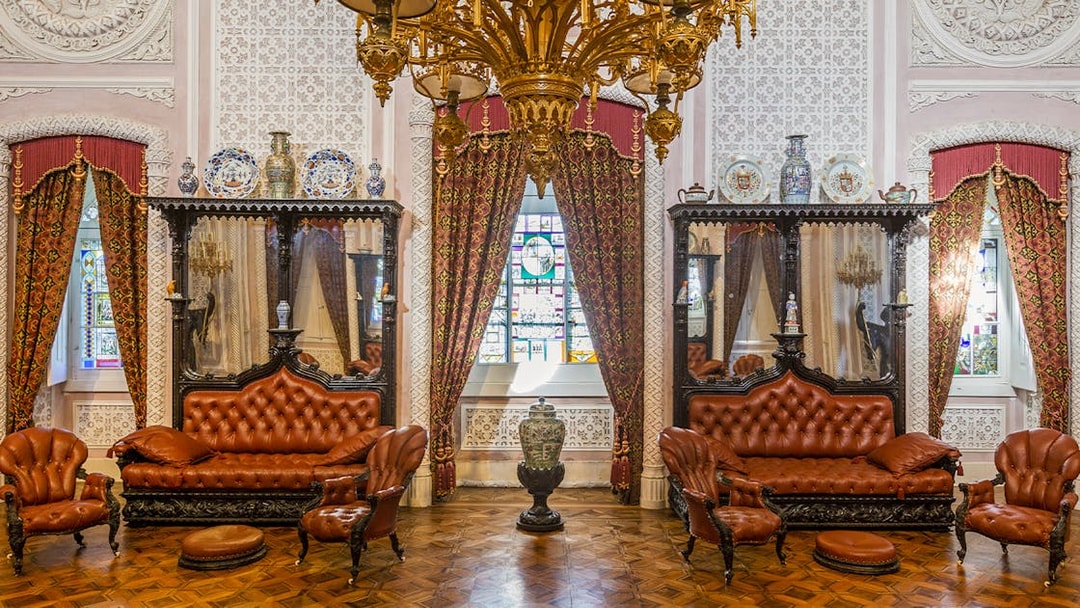 Great Hall of Pena Palace with ornate chandelier, stained glass window, and antique furniture.