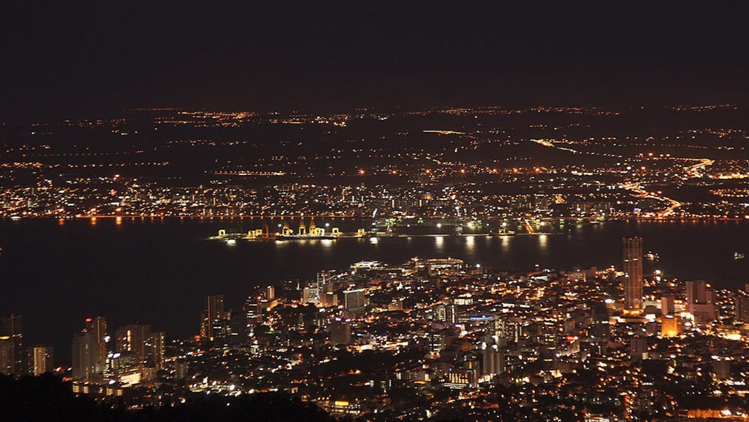 Night view of Penang cityscape from Penang Hill, Malaysia, with illuminated buildings and coastline.