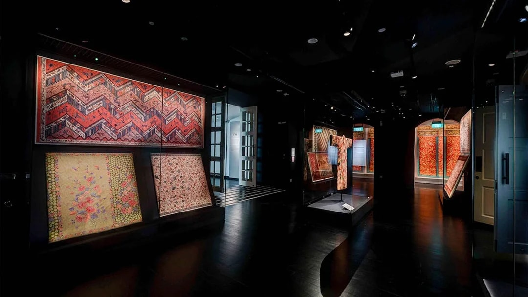 Dimly lit gallery with red and gold textiles at Peranakan Museum, Singapore.