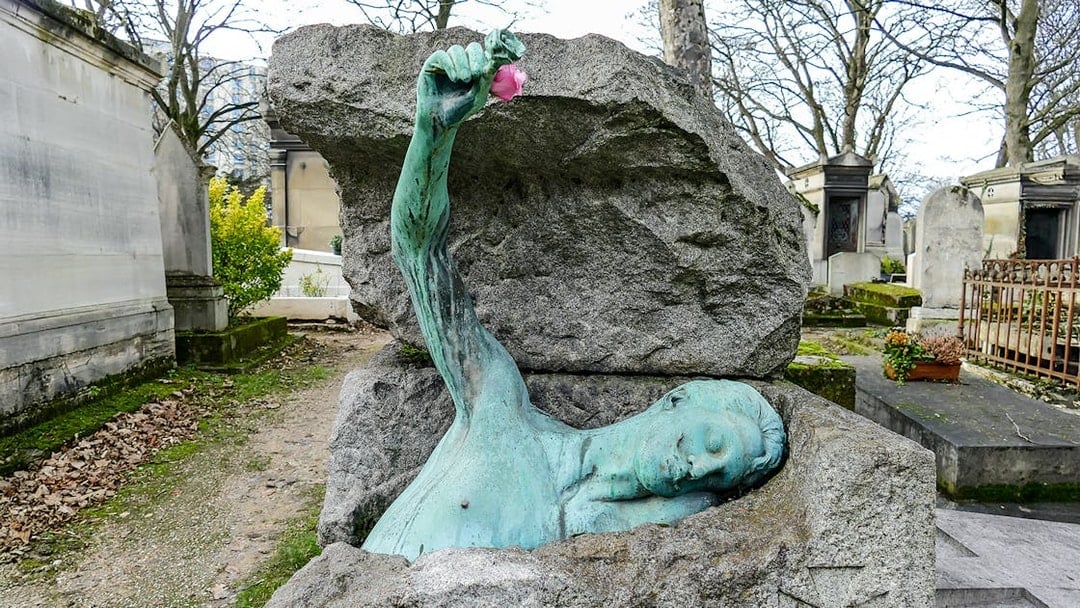 Sculpture of a figure emerging from a tomb at Père Lachaise Cemetery, Paris.