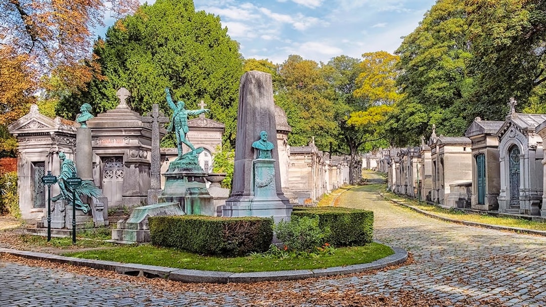 Père Lachaise Cemetery path with ornate tombs and statues, Paris.