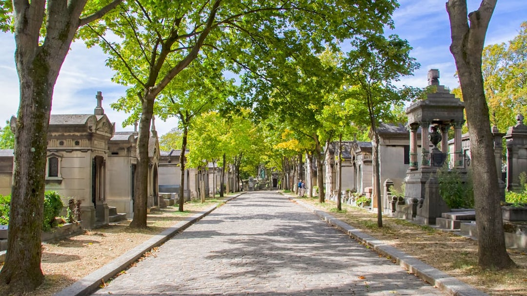 Cobbled path lined with tombs and trees at Cimetière du Père Lachaise, Paris.