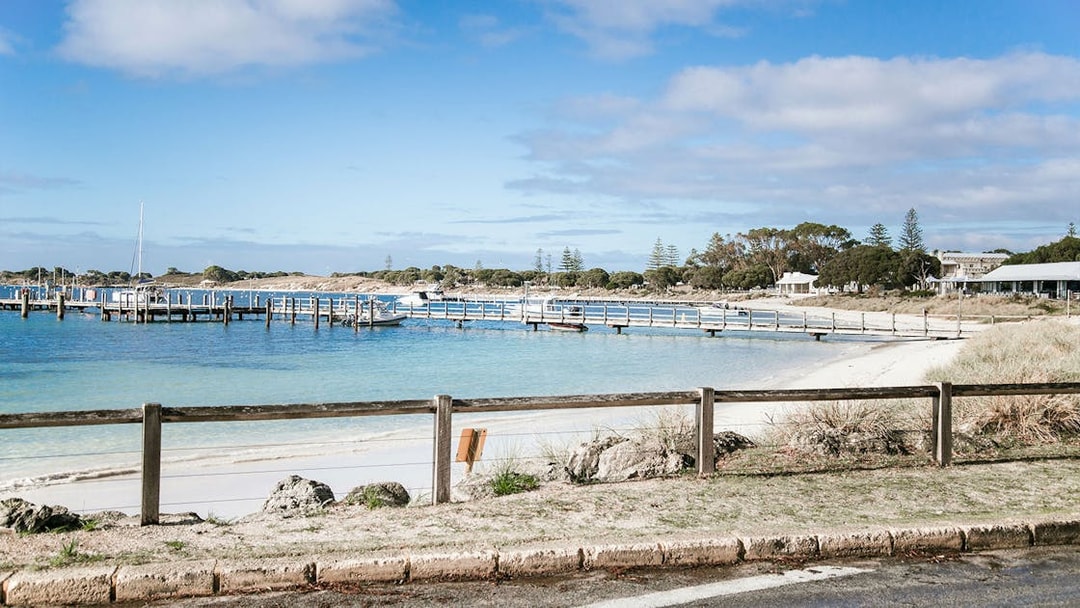 Boats docked at a pier on Rottnest Island, Australia, with sandy beach and clear blue water.