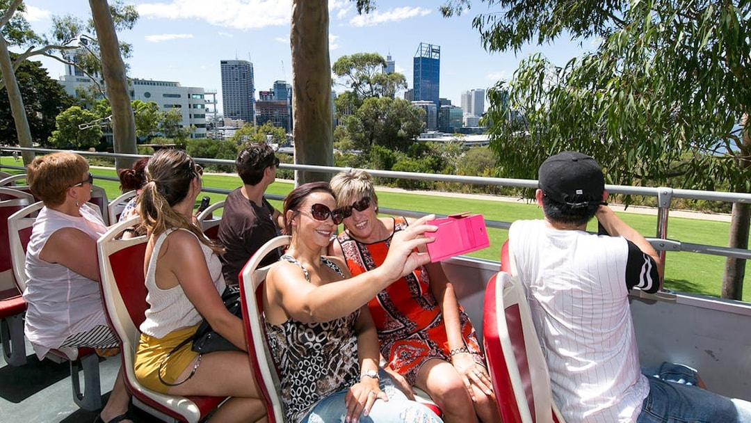 Tourists on a hop-on-hop-off bus in Kings Park, Perth, taking photos of the city skyline.