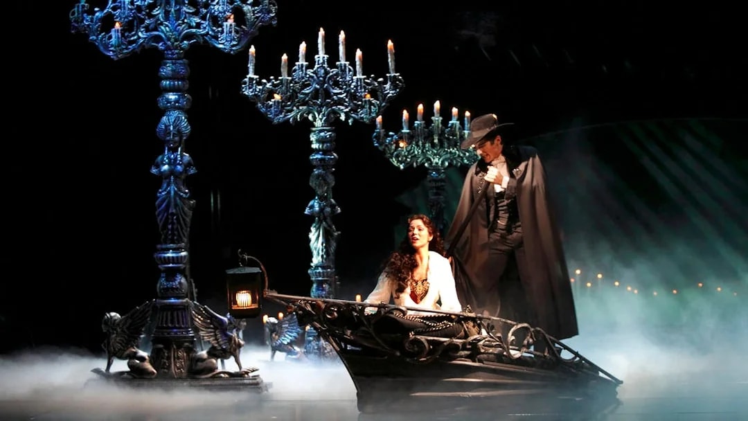 Phantom of the Opera scene with characters in a boat surrounded by candelabras.
