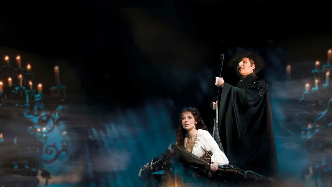 Phantom of the Opera scene with characters on a boat surrounded by candlelight.
