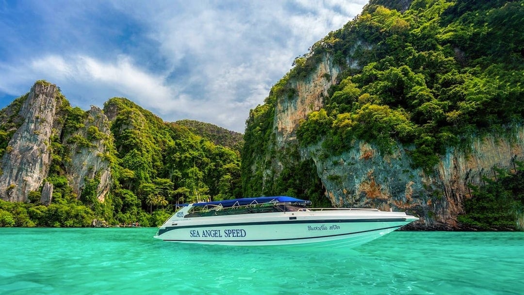 Speedboat cruising in Pileh Bay with limestone cliffs and turquoise water.