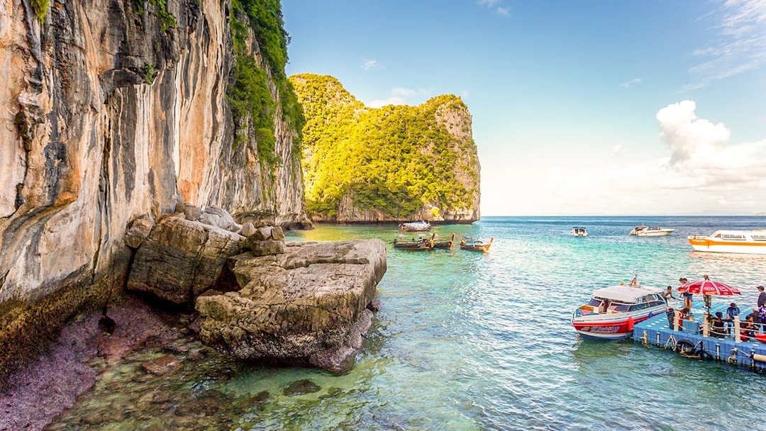 Boats docked at pier with limestone cliffs in Phi Phi Islands, Thailand.