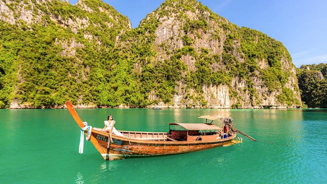 Longtail boat with woman enjoying view of Phi Phi Island cliffs and turquoise water.