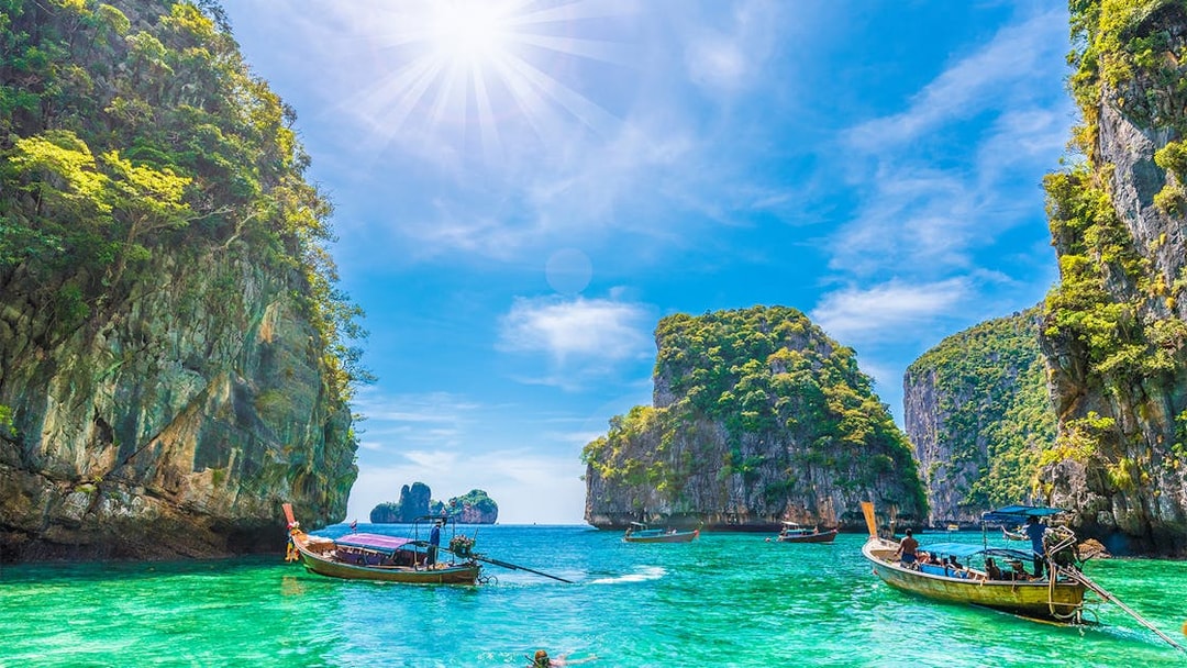 Longtail boats in Loh Samah Bay, Phi Phi, with limestone cliffs and clear water.