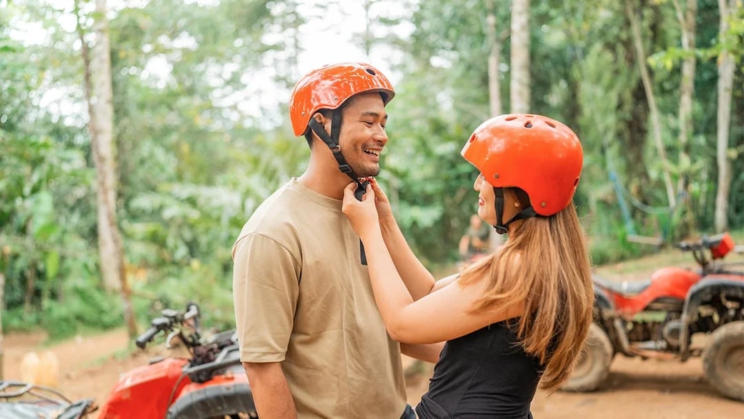 Couple preparing for ATV ride in Phuket jungle with helmets.