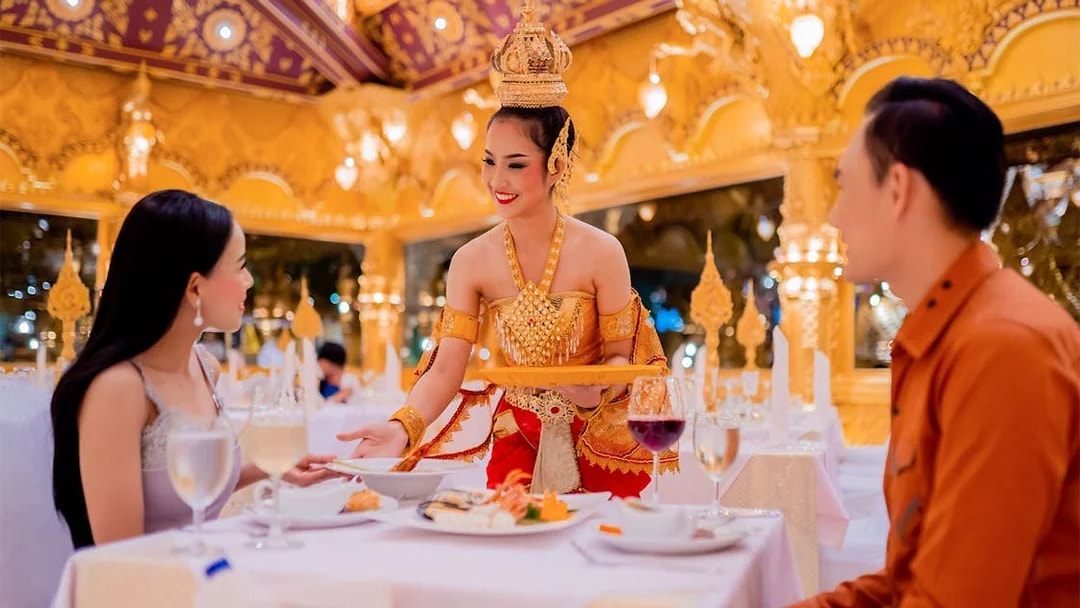 Server in traditional attire serving dinner at Phuket Fantasea with ornate golden decor.
