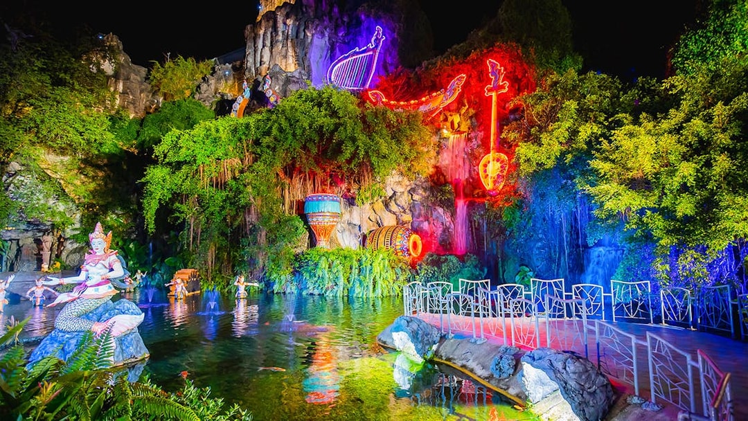 Phuket Fantasea night show with neon lights and mythical statues by a pond.