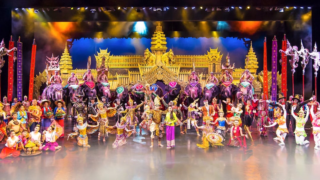 Performers in traditional costumes on stage at Phuket Fantasea with elephants and ornate backdrop.