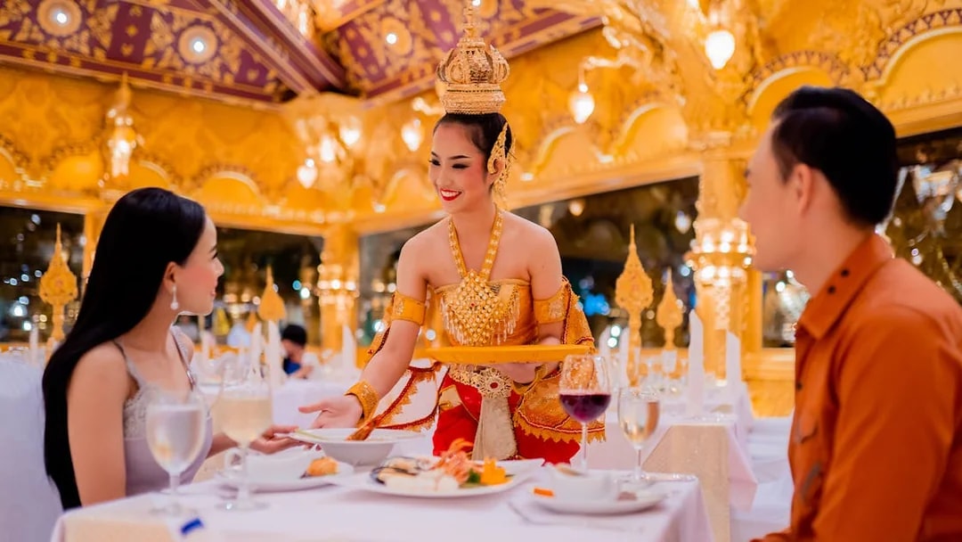 Server in traditional attire serving guests at Phuket Fantasea dinner show.