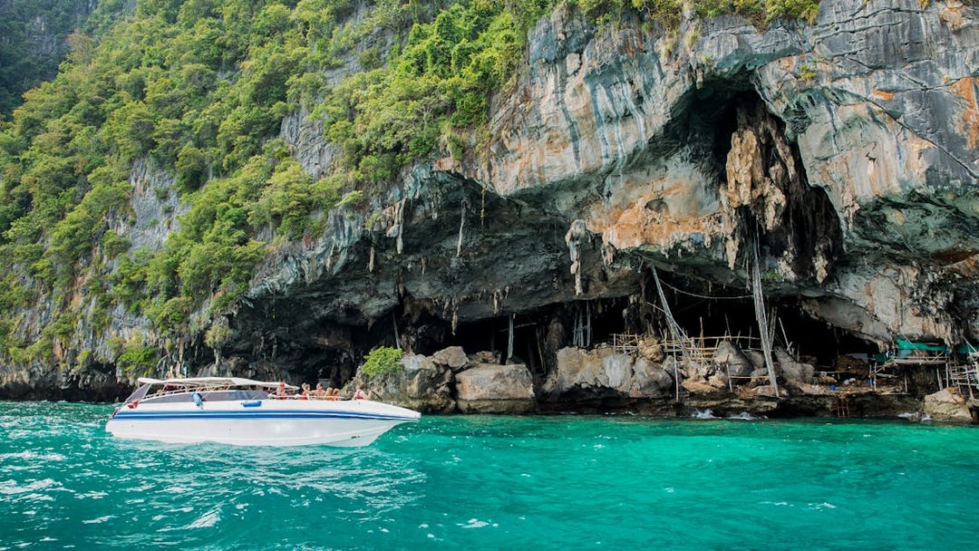 Speedboat near Viking Cave on Phi Phi Island, Thailand, with lush cliffs and turquoise water.