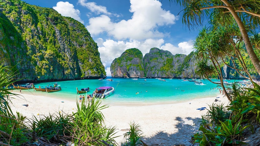 Maya Bay beach with boats and tourists, surrounded by limestone cliffs, Phuket, Thailand.