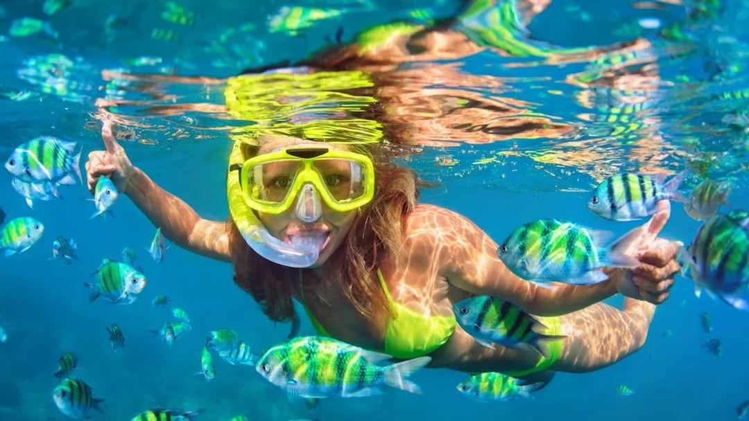 Woman snorkeling among colorful fish in clear tropical waters.