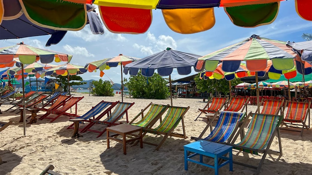 Colorful beach umbrellas and chairs on sand in Khai Island.