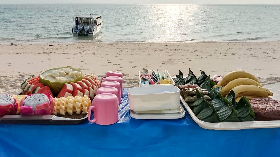 Beachside fruit and food spread with a catamaran in the background near Phi Phi.