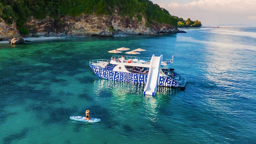 Tourist kayaking near whale shark fleet boat with slide in tropical waters.