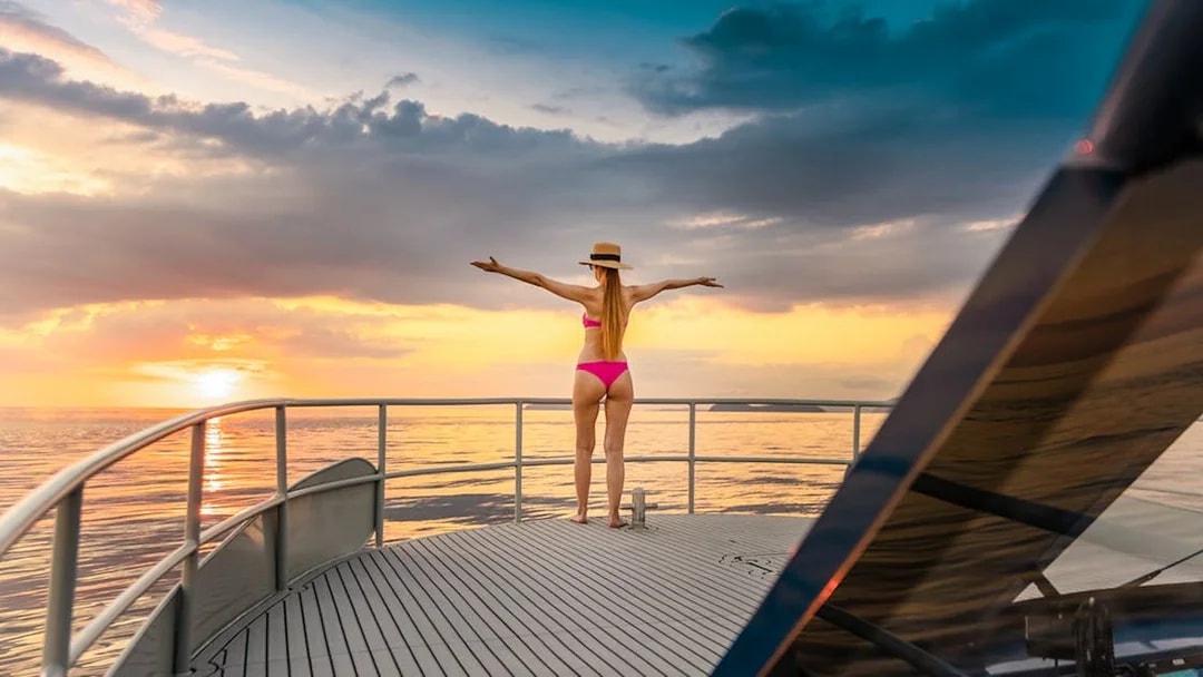 Tourist on yacht deck enjoying ocean sunset views.