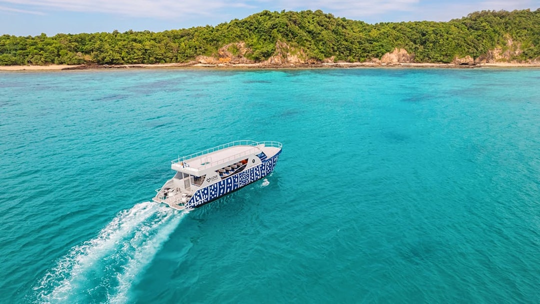 Speed boat cruising on turquoise waters near lush green island.