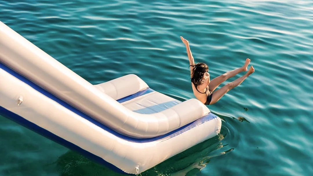 Person sliding into emerald green water from inflatable slide, surrounded by limestone mountains.