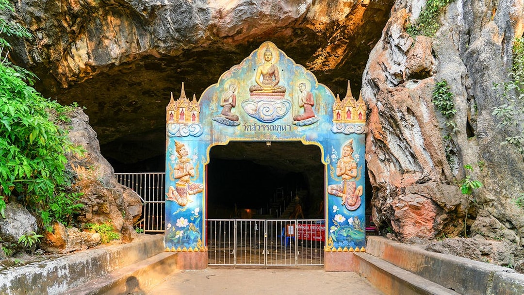 Entrance to a decorated cave temple in Phuket, featuring colorful religious artwork.