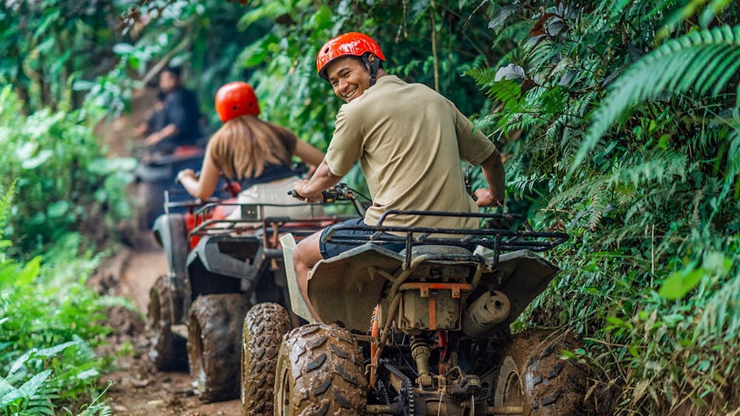 Man smiling while riding ATV through lush forest trail.