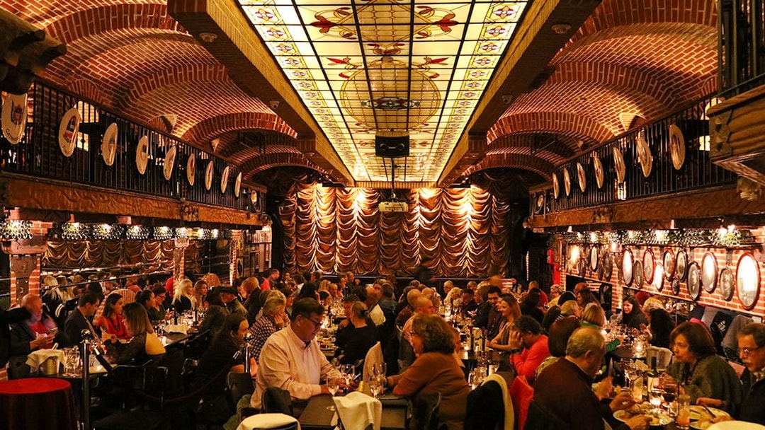 Guests dining at Piazzolla Tango Show venue with ornate ceiling and stage in Buenos Aires.