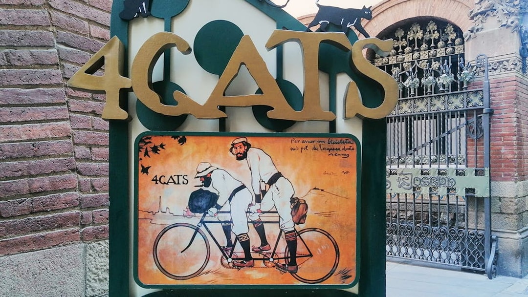 4 Gats sign in Barcelona, featuring artwork of two men on a tandem bicycle, part of Picasso walking tour.