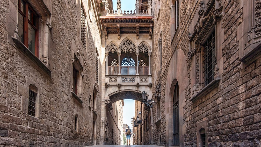 Visitor exploring the Gothic Quarter's narrow street under the Bishop's Bridge in Barcelona.