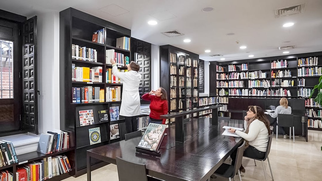 Library interior of the Picasso Museum in Malaga with people reading and browsing books.
