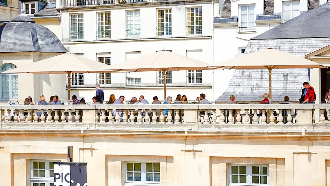 Terrace cafe at Picasso Museum, Paris, with people dining under umbrellas.