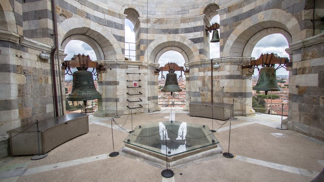 Bells inside the tower of Pisa, Italy, with city view through arches.