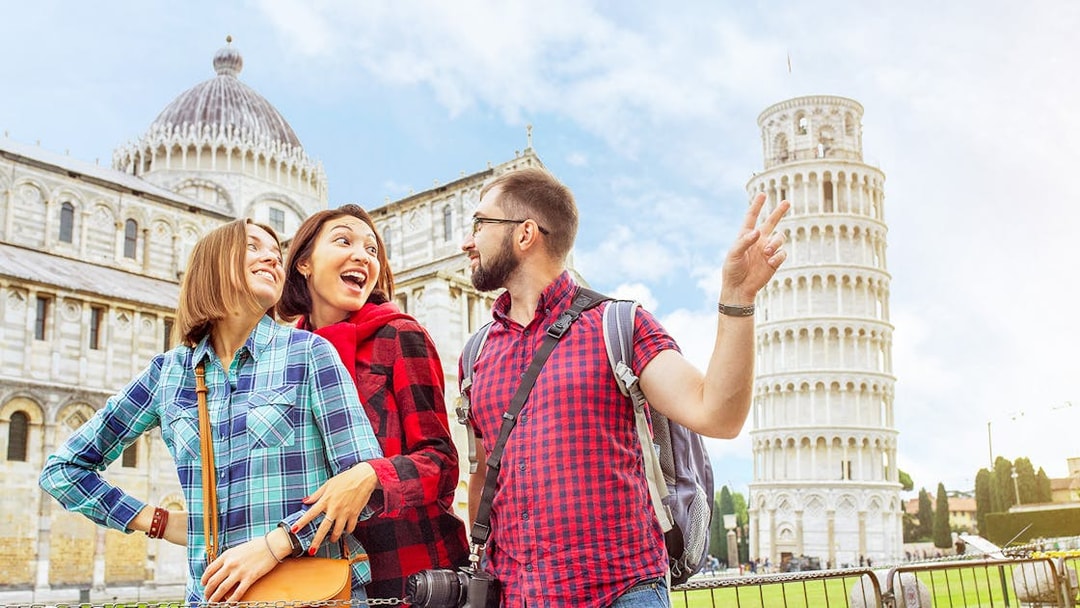 Tourists enjoying a guided tour at the Baptistery and Cathedral with the Leaning Tower of Pisa in the background.