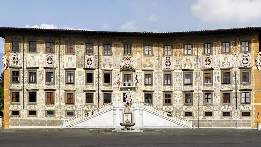 Facade of Palazzo della Carovana in Pisa with ornate sculptures and detailed frescoes.