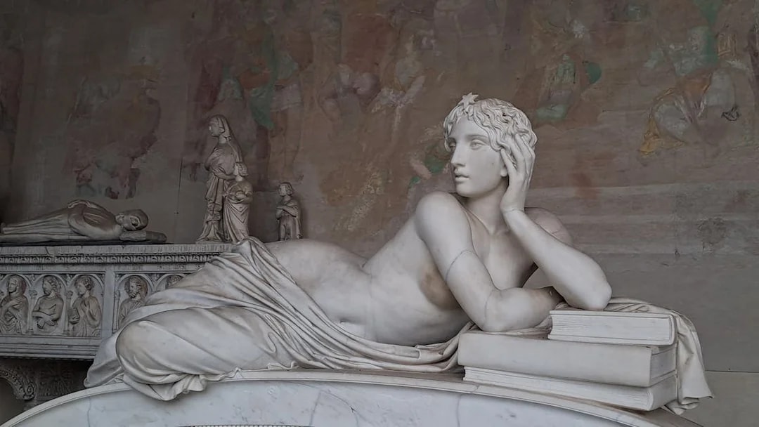Marble statue in Pisa's Field of Miracles, depicting a reclining figure with books.