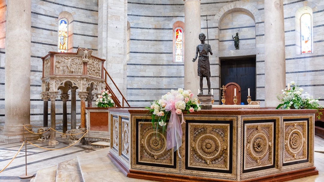Baptistery of Pisa interior with ornate pulpit and floral decorations.