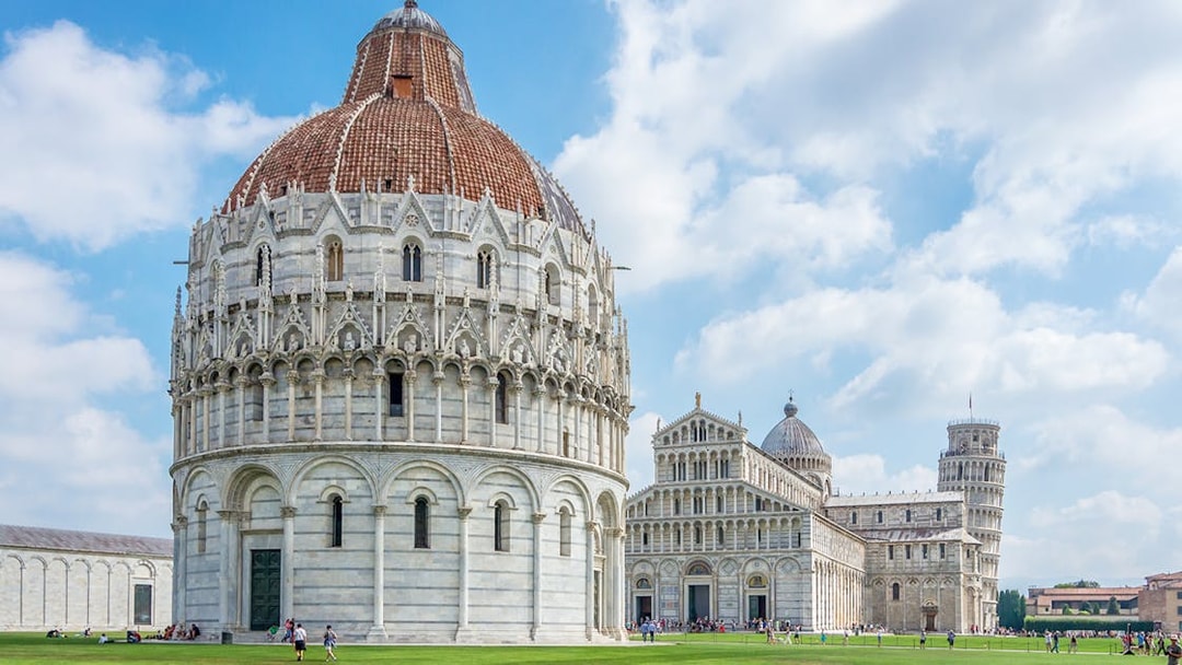 Baptistry of San Giovanni exterior with Pisa Cathedral and Leaning Tower in background.