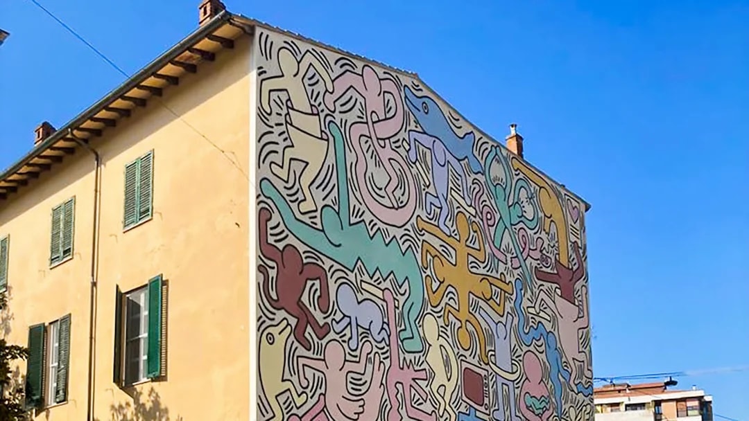 Colorful mural on a building in Pisa, Italy, featuring abstract figures and shapes.