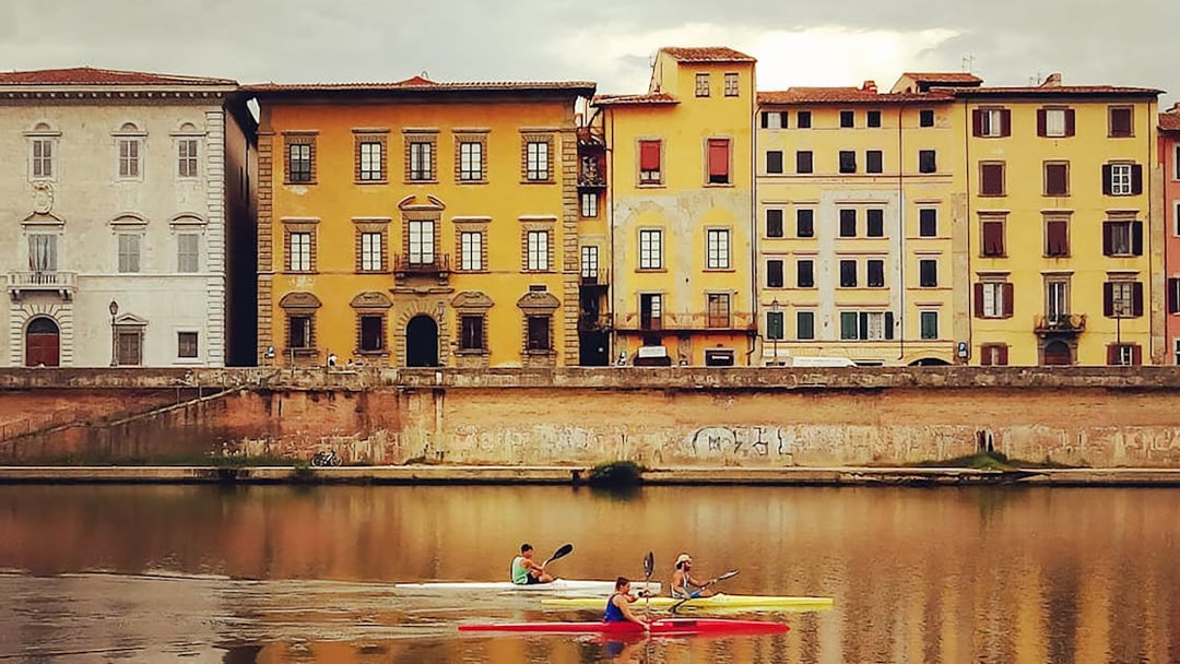 Kayakers on the Arno River with historic Pisa buildings in the background.