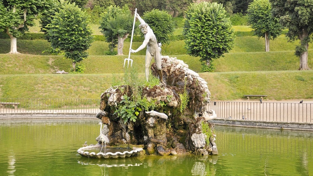 Statue of Neptune in Boboli Garden fountain, Florence, Italy, surrounded by greenery.