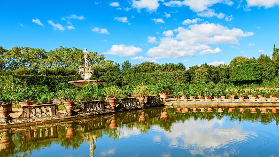 Fountain and statues in the Boboli Gardens, Florence, with surrounding greenery and reflection in water.