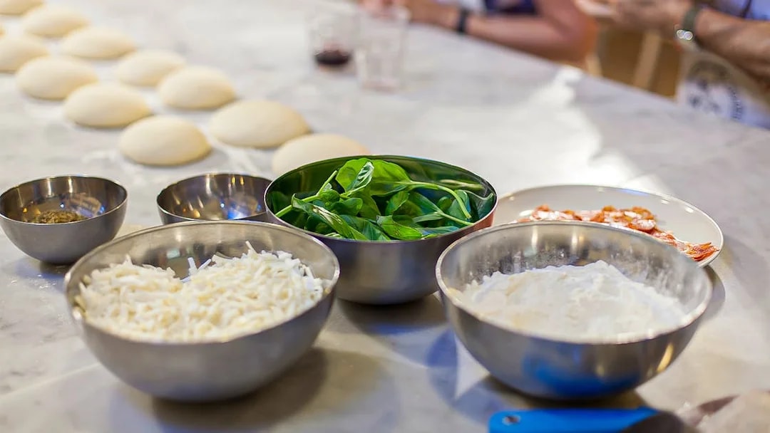 Pizza ingredients on a table for a cooking class, including dough, cheese, and basil.