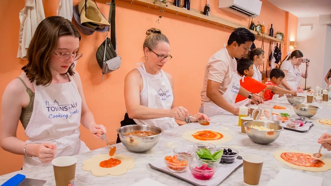 Participants making pizza dough in a cooking class, with toppings and sauce on a table.