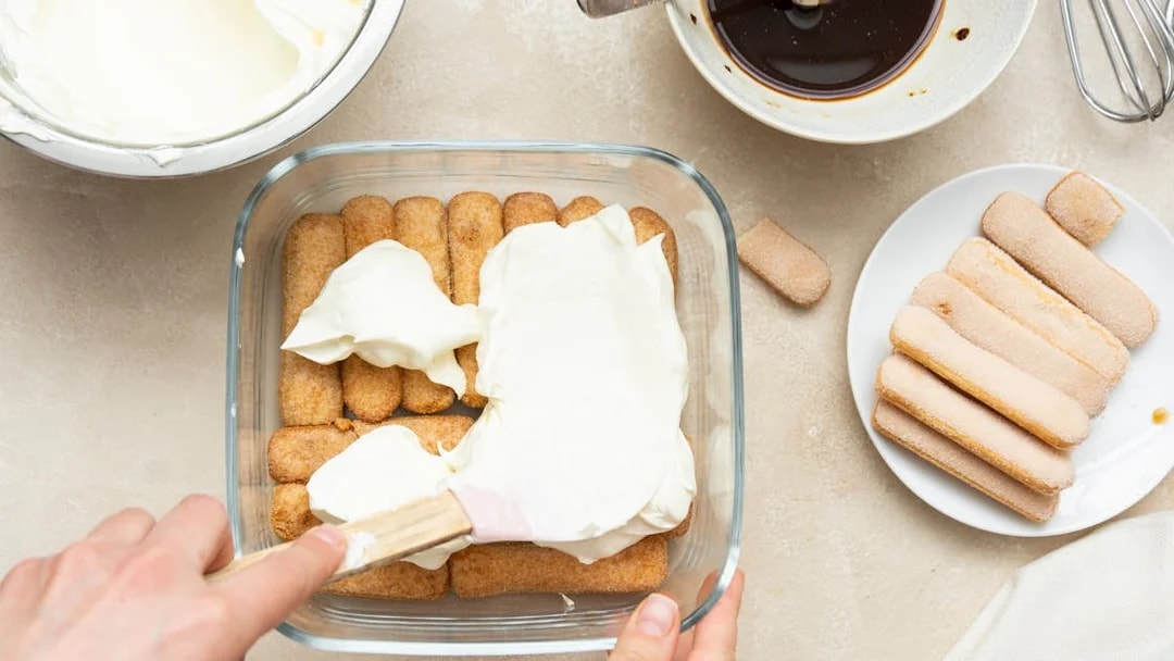 Spreading mascarpone over ladyfingers for tiramisu preparation.